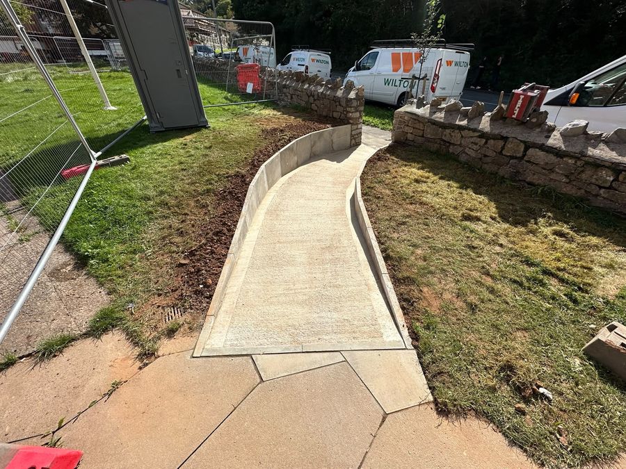A concrete access ramp curving between new stone retaining walls