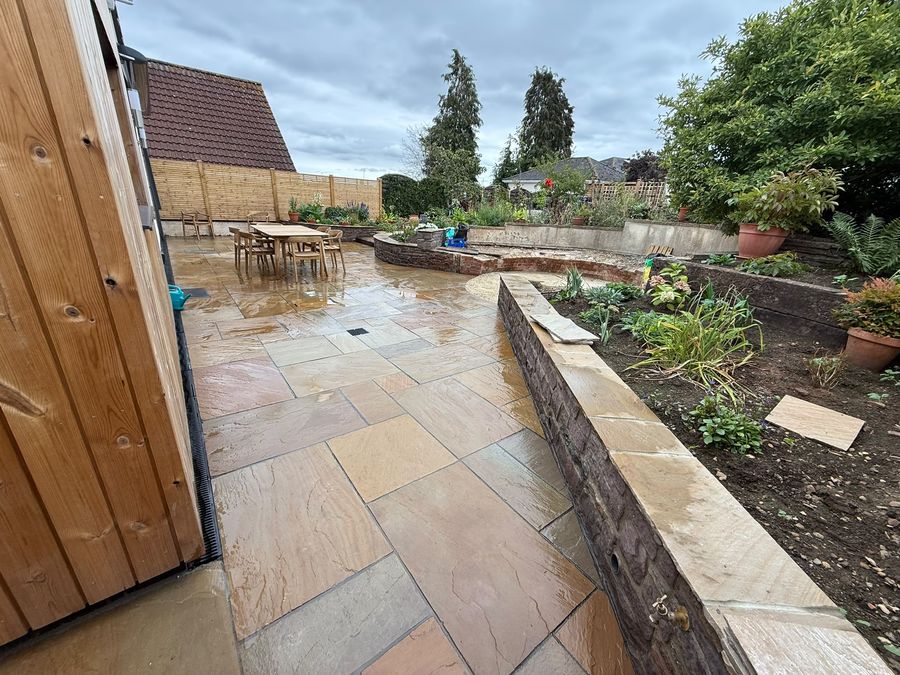 A sandstone patio laid between raised beds, with a low retaining wall along one side