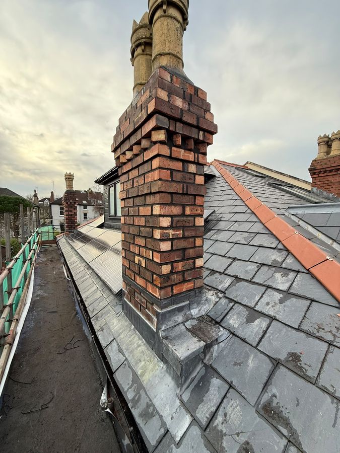 A chimney stack rebuilt in red brick above a slate roof, with new pots set on it