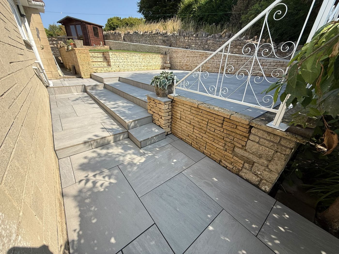 Sawn grey paving and steps rising to an upper terrace between coursed
                stone retaining walls, with a dry stone wall behind
