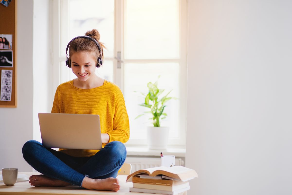 A smiling girl in headphones sitting cross-legged with her laptop