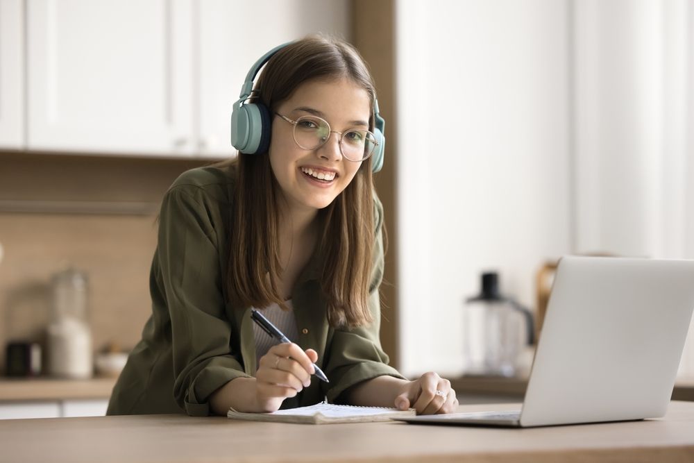 A teenage student in headphones making notes at her laptop