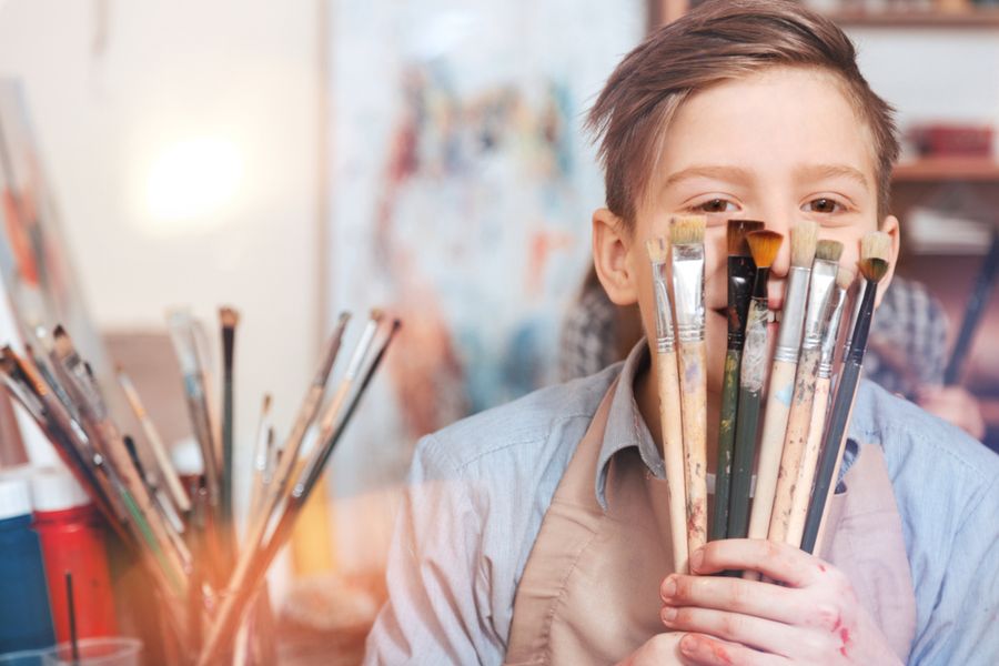 A boy holding a bunch of paintbrushes
