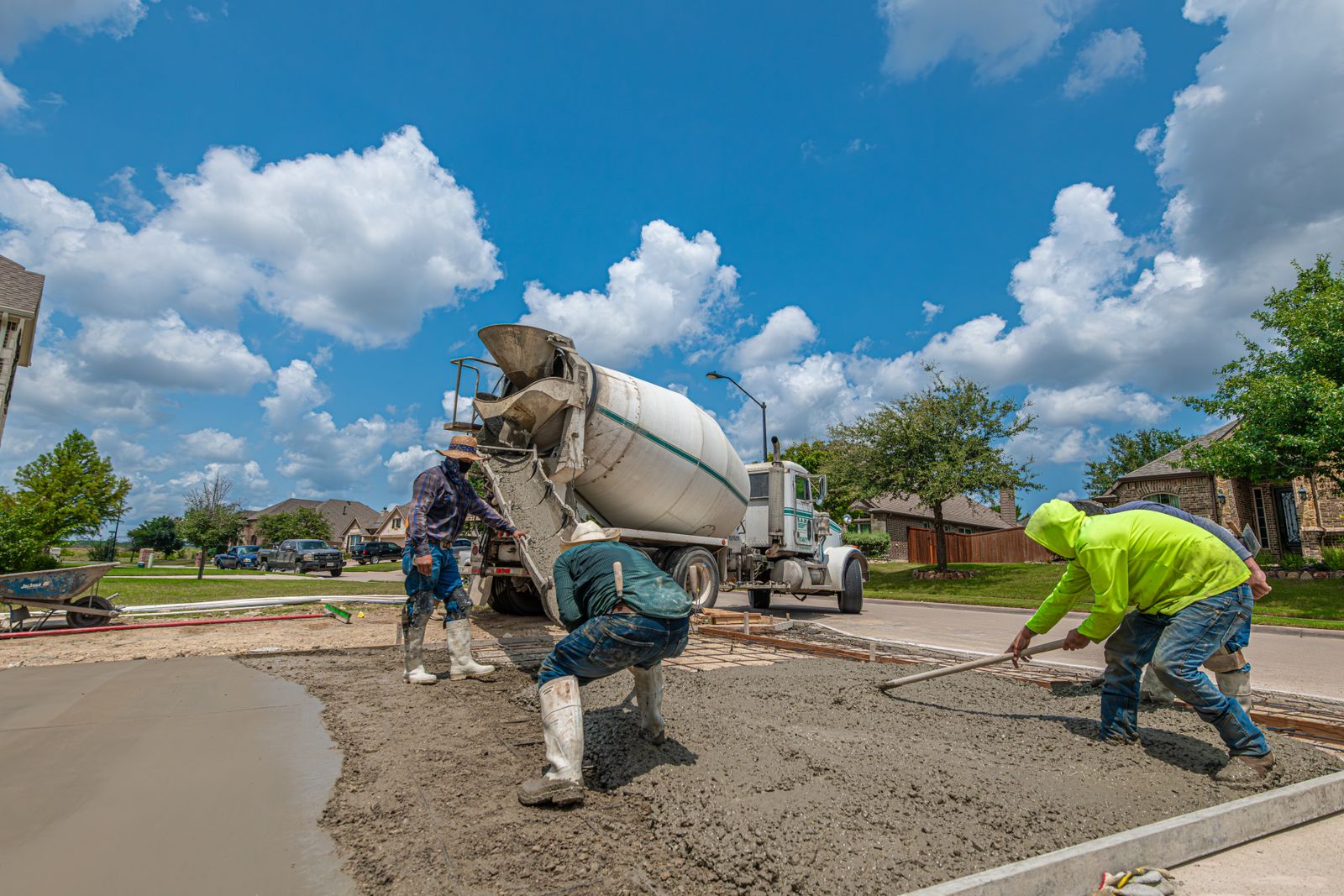 Concrete being discharged from a mixer truck onto a house driveway while two workers rake it level