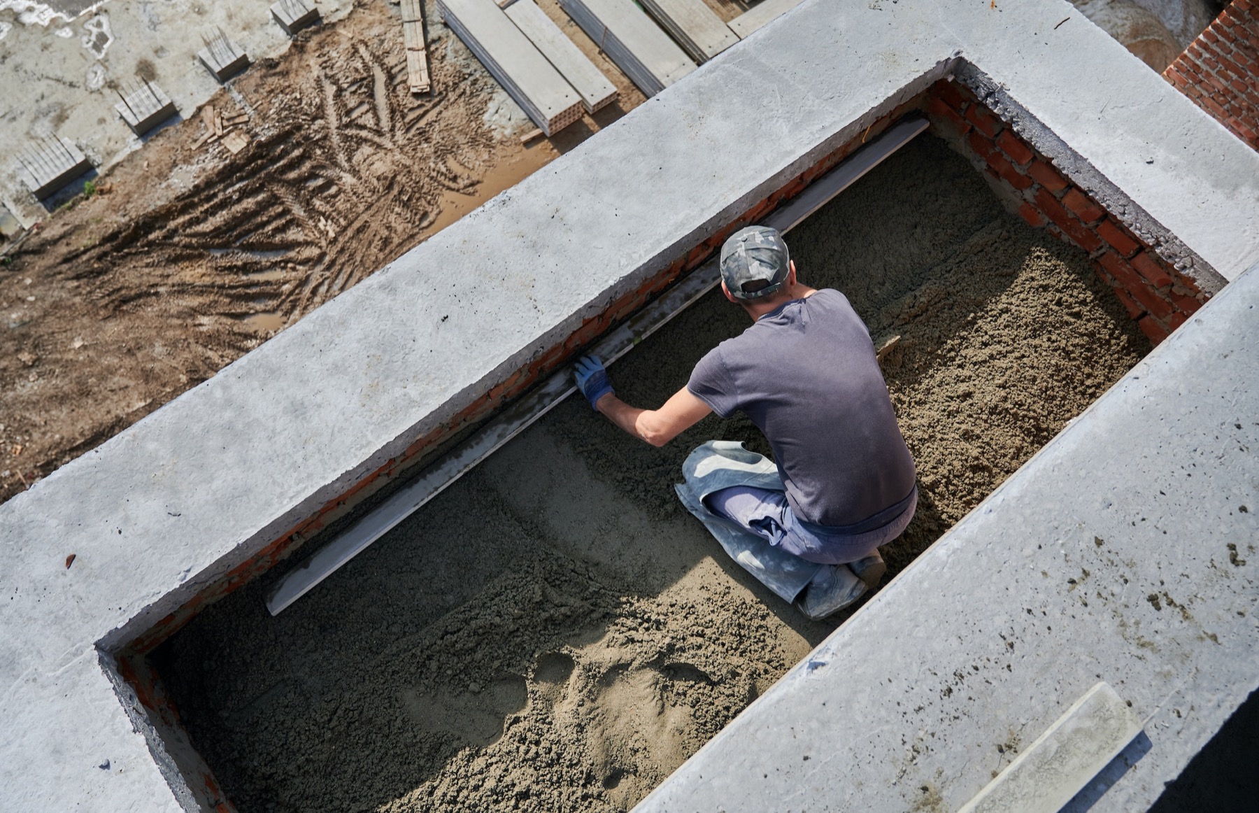 A worker levelling floor screed with a straight edge inside a partly built house