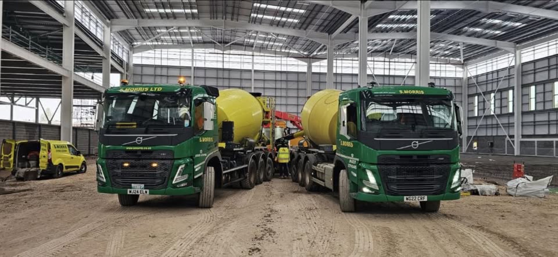 Two S. Morris Volvo mixers and a company van inside a steel-framed building under construction