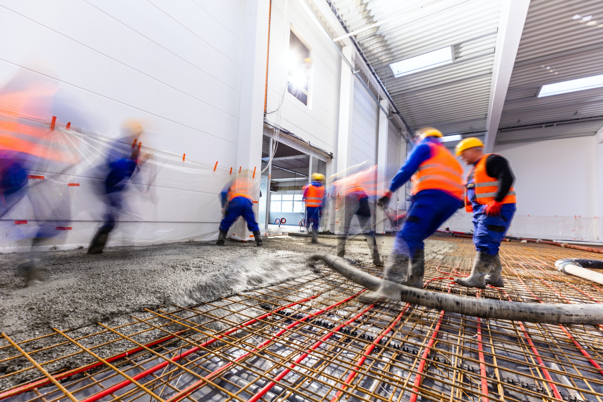 Screed being pumped and levelled over underfloor heating pipes and steel mesh in a warehouse floor