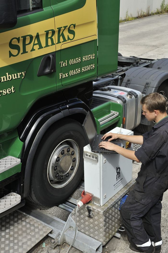 A Sparks driver carrying out checks beside a truck's front wheel