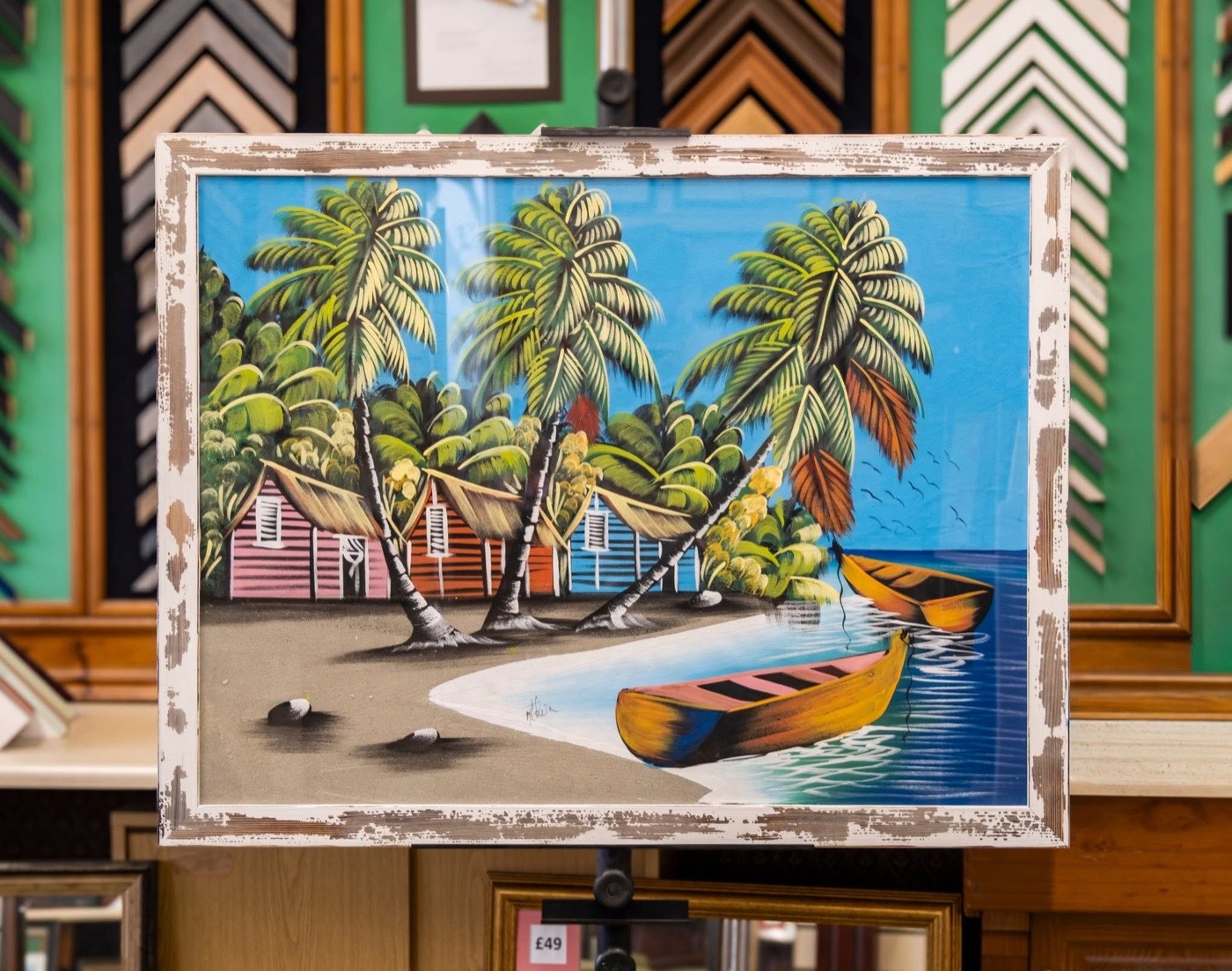 A beach painting framed in a distressed white moulding, on an easel in the Weston Super Frames gallery