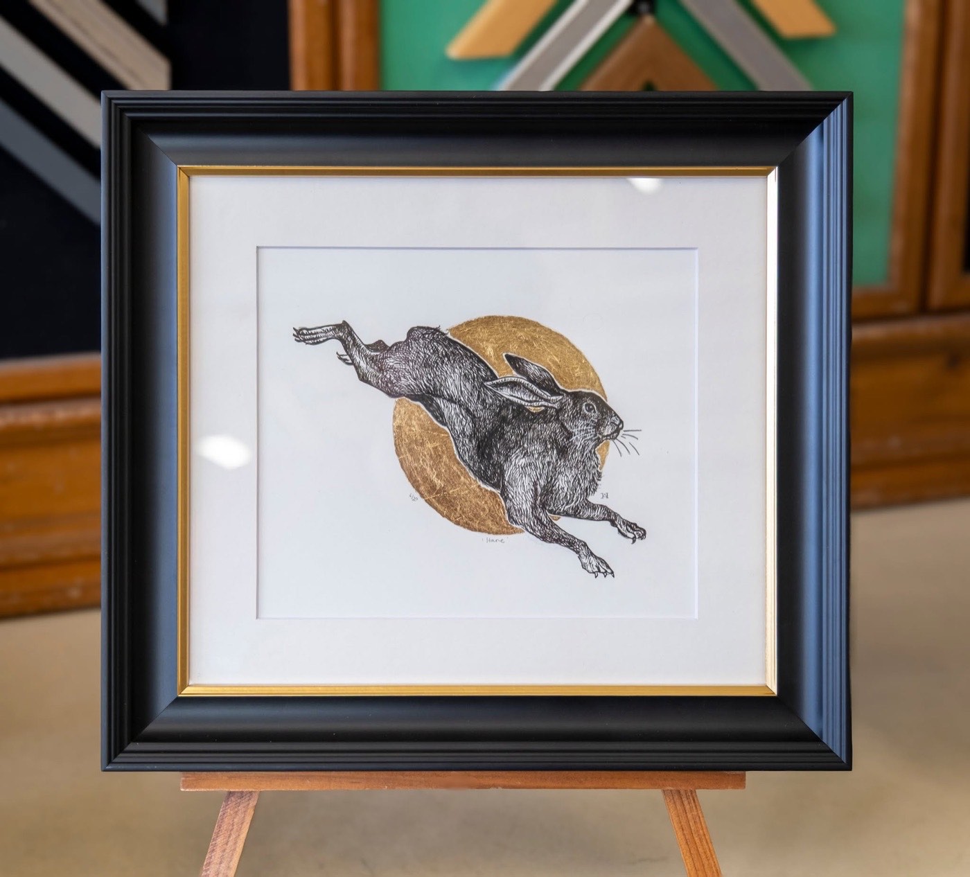 A limited edition hare linocut with gold leaf, framed in black with a gold slip and a white mount