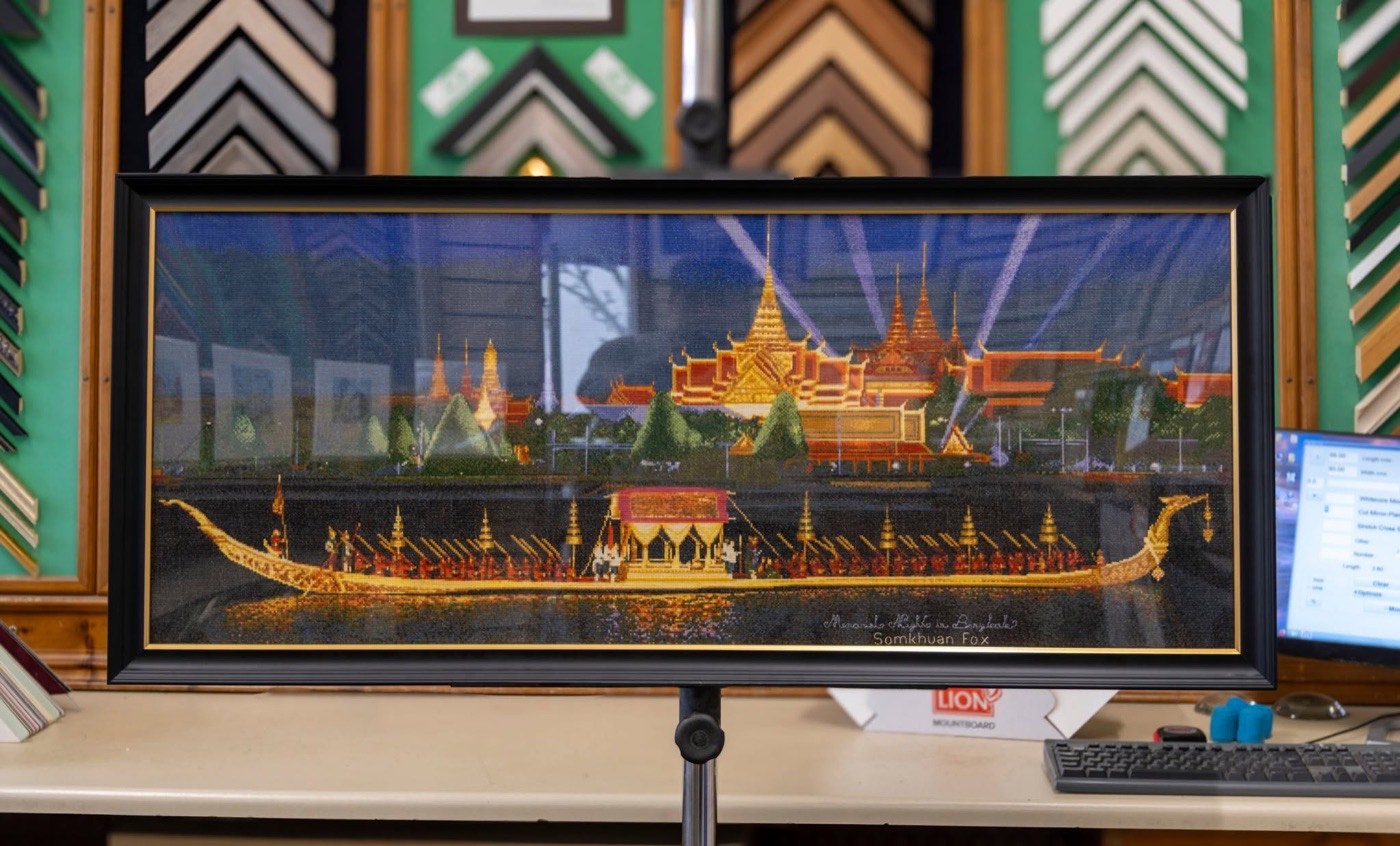 A panoramic cross stitch framed in black with a gold slip
